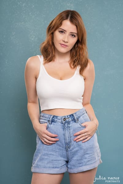 Melbourne Actor headshot of girl in white singlet and denim shorts on a blue background.