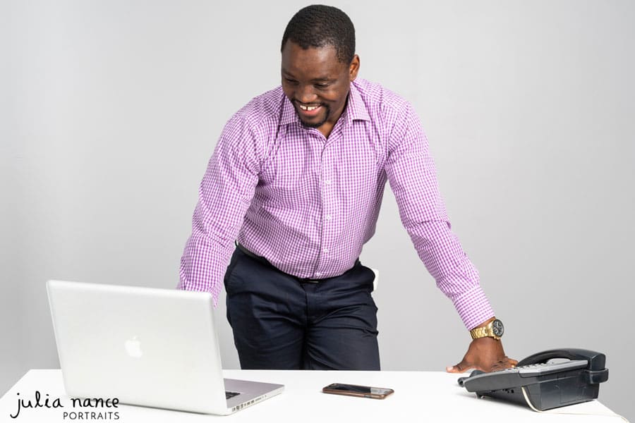 Melbourne corporate headshot photography and personal branding portraits. Man standing at desk smiles for promotional portraiture
