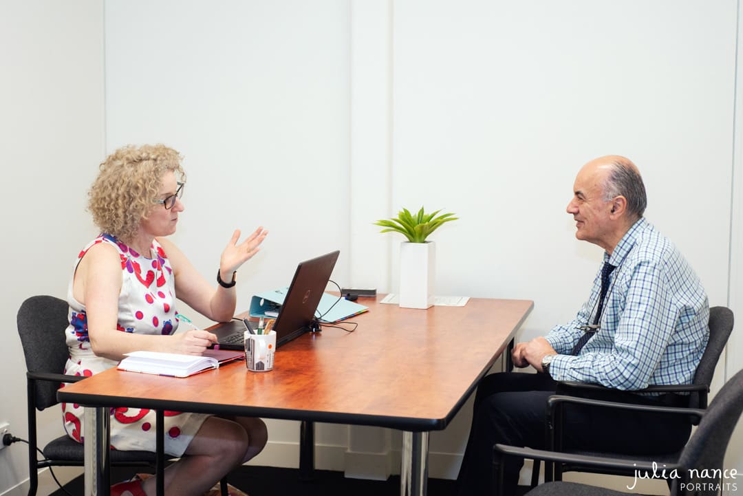 Personal branding photography of two people having a meeting while sitting at a desk. On-site corporate portrait photograph taken by Julia Nance Portraits