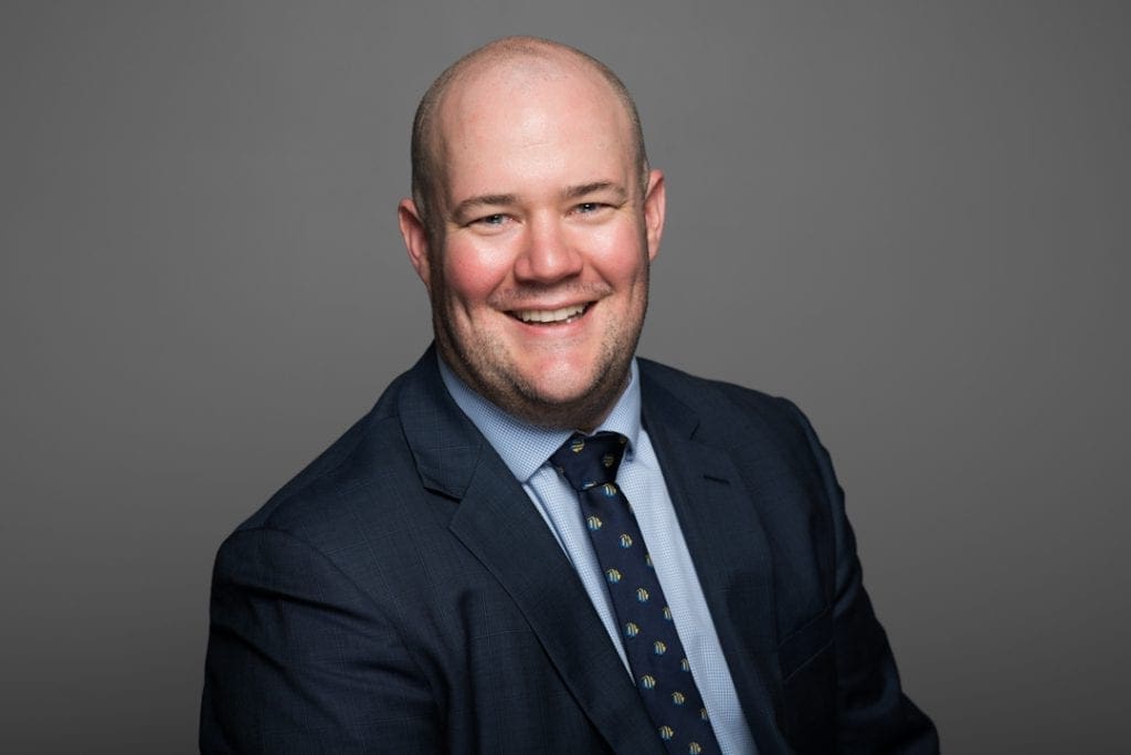 Melbourne corporate headshot of man smiling on grey background wearing a suit and tie for a LinkedIn headshot