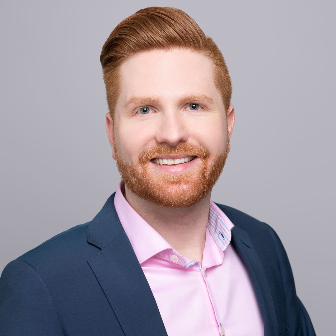 Corporate headshot of man wearing pink shirt and blue blazer, smiling at the camera.