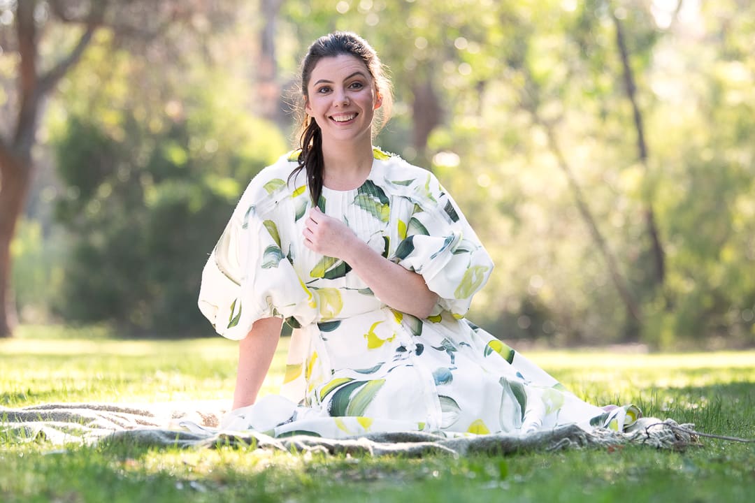 A personal branding portrait of a woman sits outside in a natural outdoor setting in melbourne and smiles to camera.