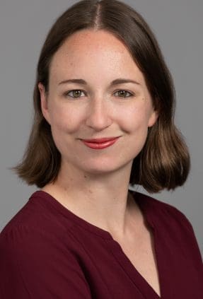 Professional corporate headshot of woman smiling softly to camera on a grey background.