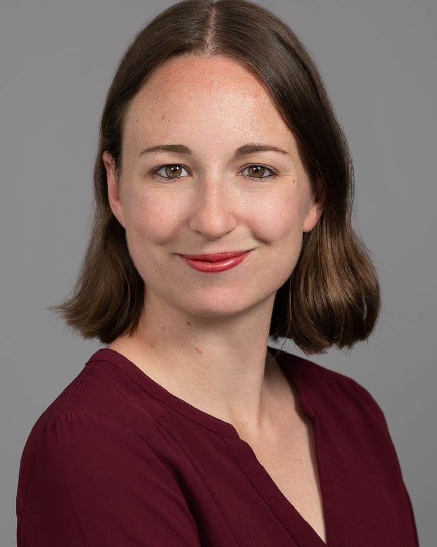 Professional corporate headshot of woman smiling softly to camera on a grey background.