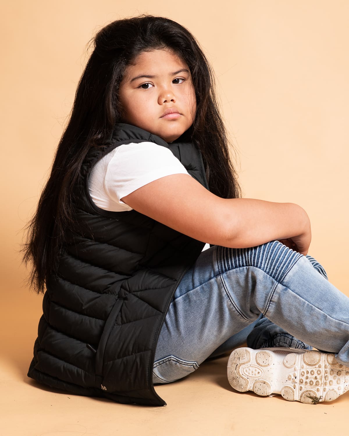 Melbourne youth actor for an actor headshot portfolio update. Girl sits on an earthy orange background in studio in a relaxed pose wearing streetwear fashion.