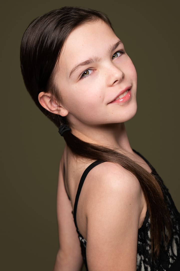 Melbourne actress and dancer looks over her shoulder on an olive green background for a captivating studio headshot.