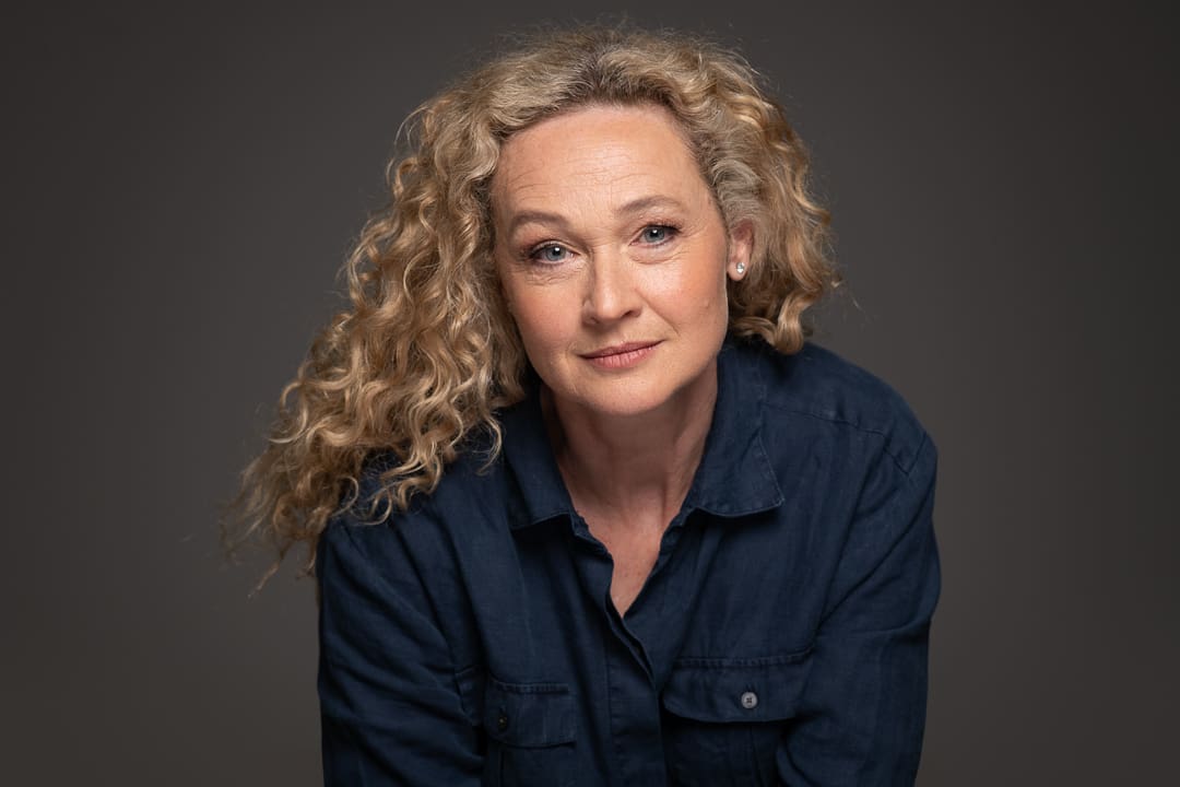 A captivating actor headshot of mature melbourne actress Angela, who leans in towards the camera with a very slight smile.