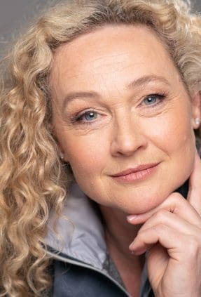 Actor headshot of Melbourne woman looks directly to camera with her hand under her chin.