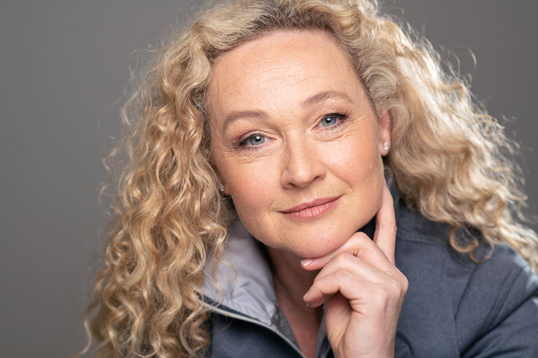 Actor headshot of Melbourne woman looks directly to camera with her hand under her chin.