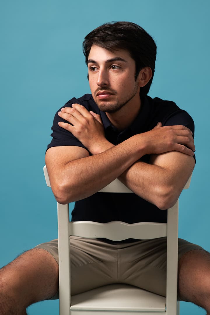 Model portfolio capture of melbourne man straddling a chair and leaning over the back, he is looking away from the camera.