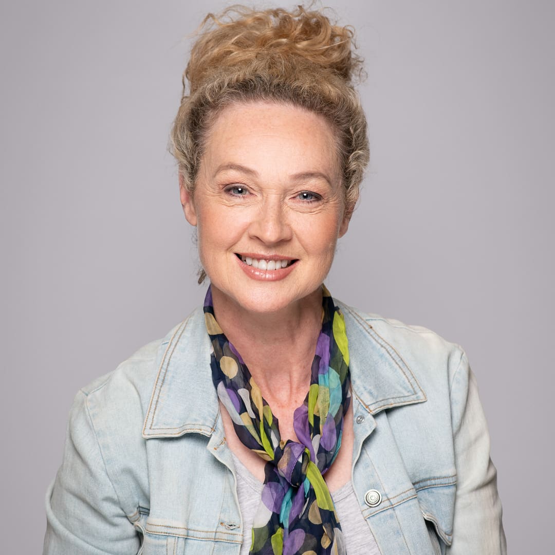 Actor headshot of woman wearing a colourful patterned scarf, light blue denim jacket, with her hair up.