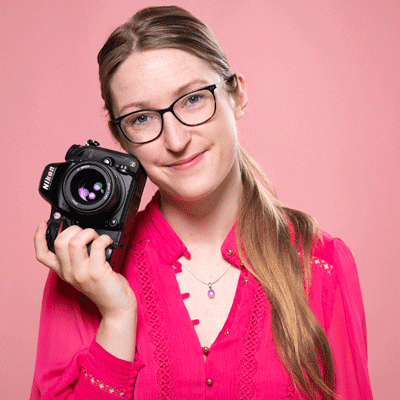 A moving gif of headshots of Julia Nance. She holds her camera in all of them and they cycle through various expressions (from silly to smiling), on pink and blue backgrounds.