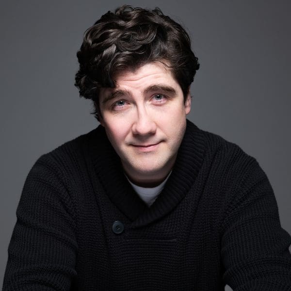 Headshot of melbourne actor Peter, who looks to camera with a slight smile. He wears all black and is photographed in a studio.