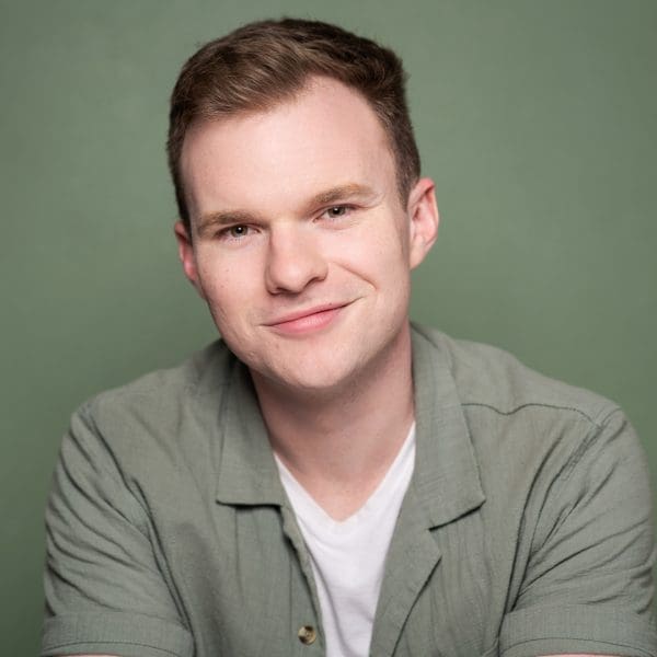 Melbourne actor headshot taken in studio on a green background. Aaron has a relaxed smile and wears a combination of green and white, creating a cohesive and striking result.