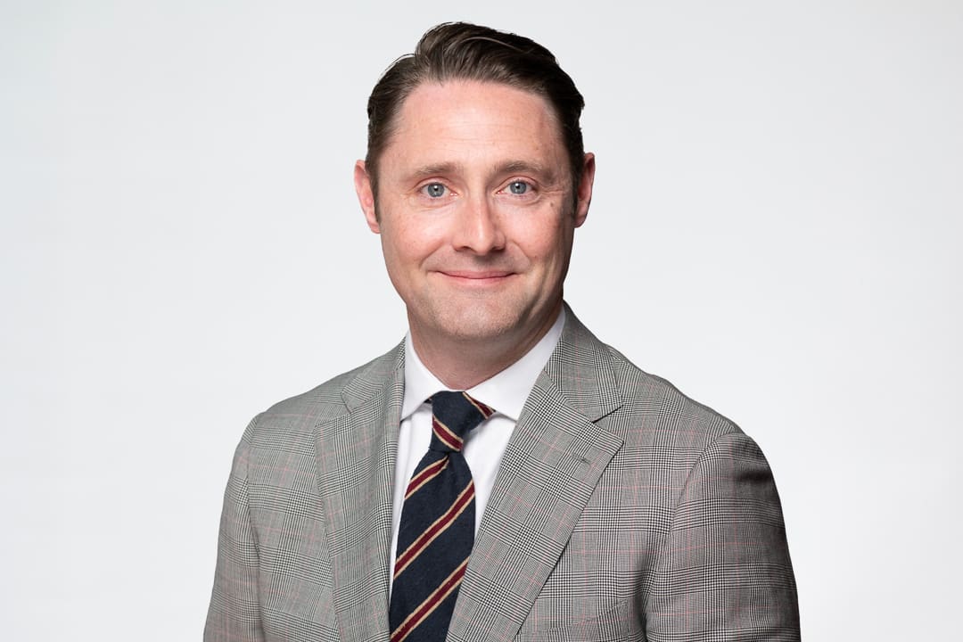 Melbourne barrister headshot of man wearing a grey checked blazer, smiling to camera confidently.