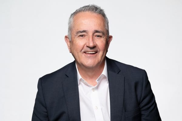 Relaxed barrister headshot of melbourne man smiling to camera, wearing a navy blazer and white shirt, with no tie.