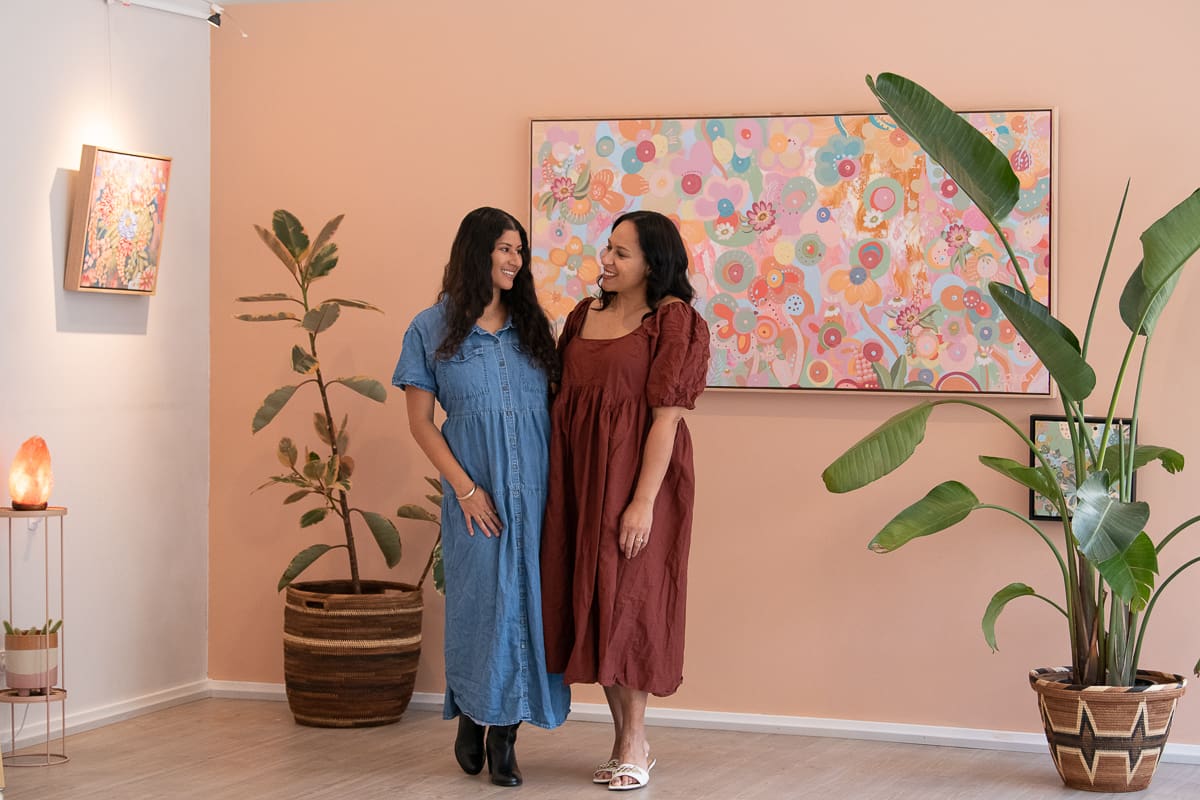 relaxed business headshot of local melbourne artists Lani and Zara, standing in front of their art work in their gallery space.