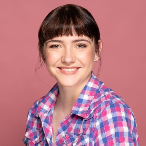 Studio actor headshot of young Melbourne woman smiling to camera wearing pink checks on a pink background.