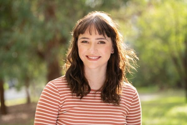 Headshot of Melbourne actor, outside using natural light. Young woman is smiling to camera with the wind blowing through her hair.