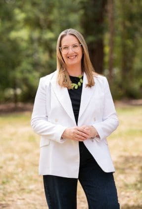 Corporate CEO portrait of woman in outdoor setting, while wearing a white blazer. She smiles to camera.