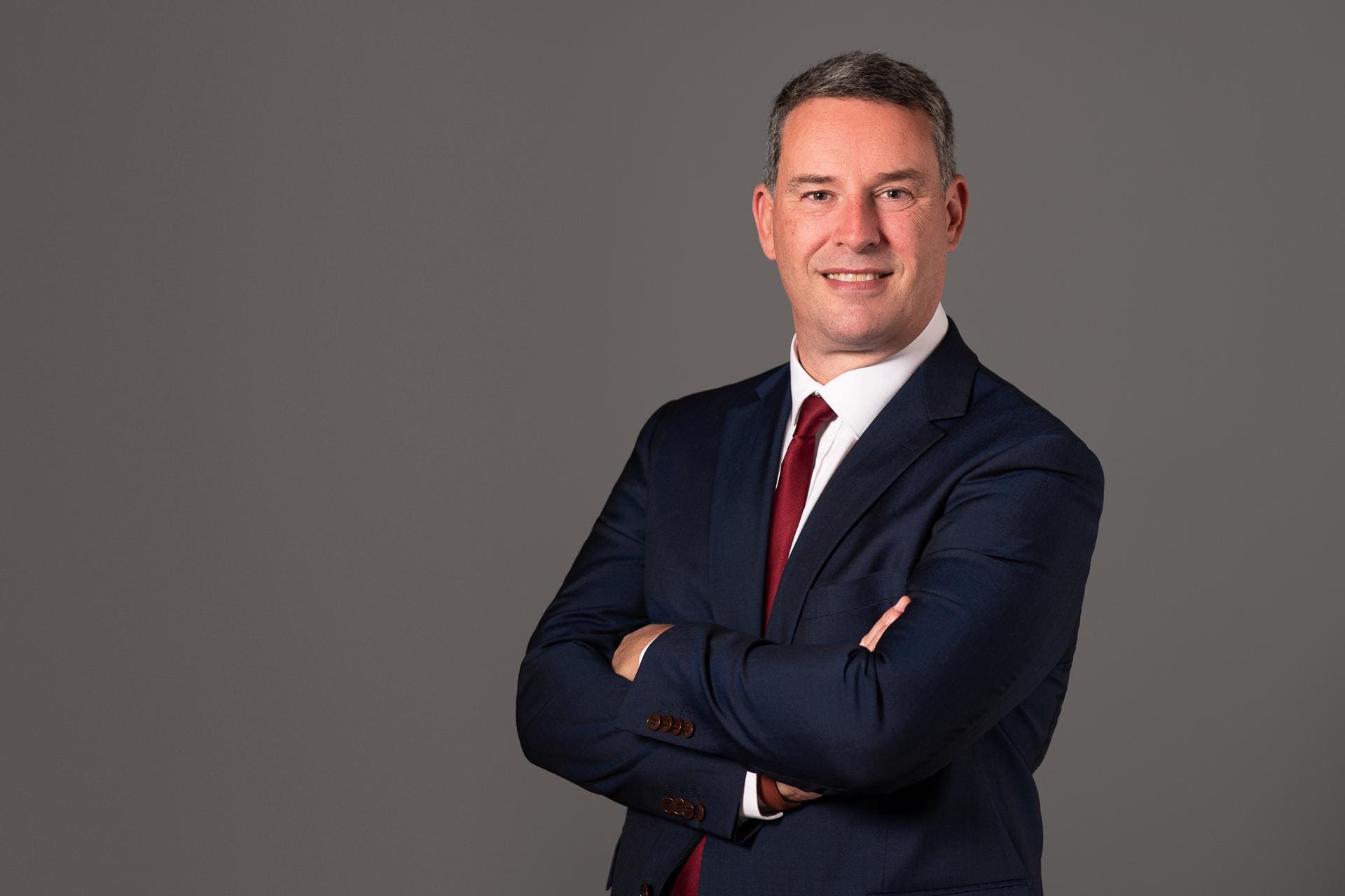 Man stands with his arms crossed for corporate portrait in studio on a grey background.