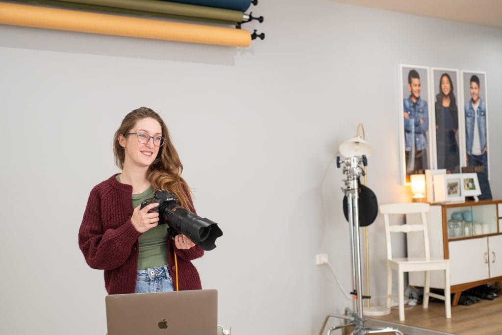 Julia Nance Holds a camera and is photographed with her laptop, mid-photography session.