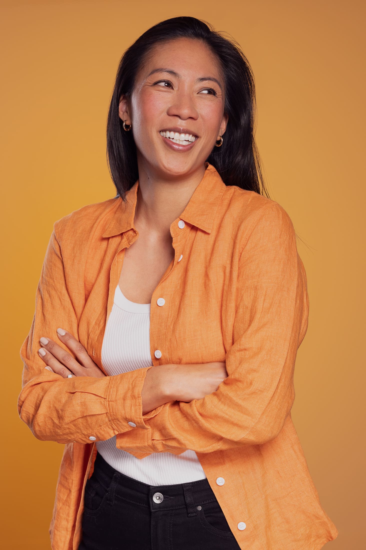 Woman laughs away from camera, with her arms crossed. She has a light orange shirt and is photographed on a yellow background.