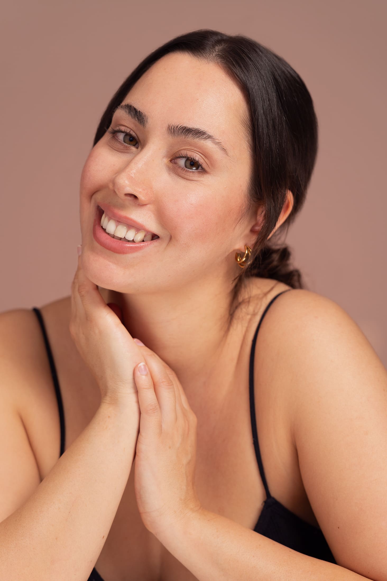 Woman smiles to camera in head and shoulders beauty portrait.