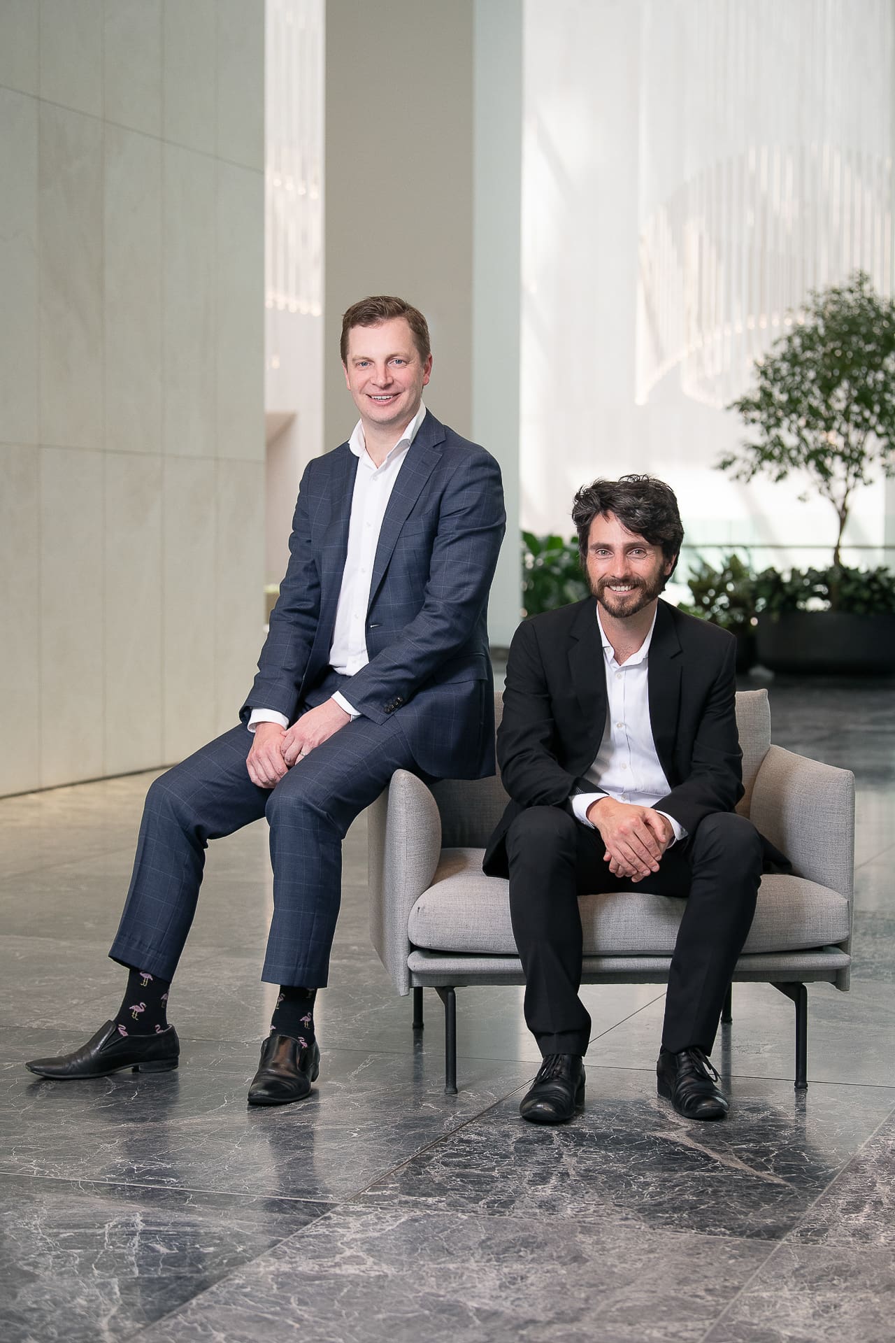 Two executive lawyers in a corporate group portrait, both seated in a high end interior.