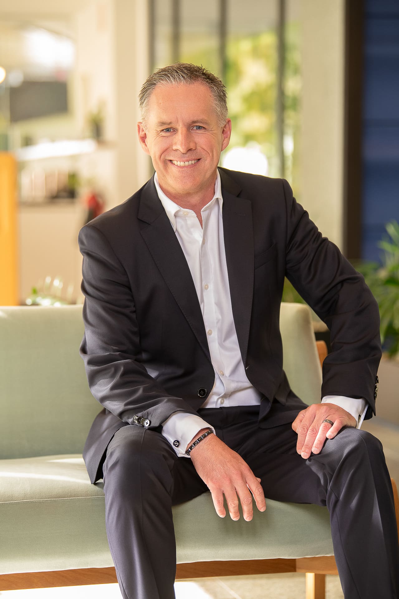 CEO portrait in a modern, bright office environment. He sits in a relaxed pose and smiles to camera with an approachable feel.