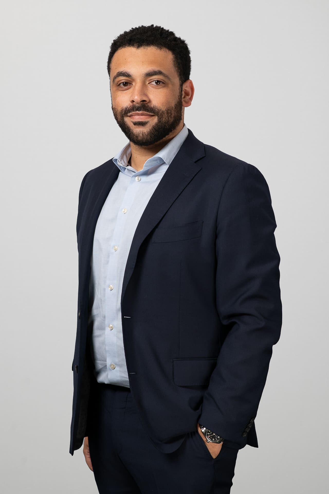 Executive portrait of a man standing to camera with his hands in his pockets, with a an almost neutral, but smiling expression