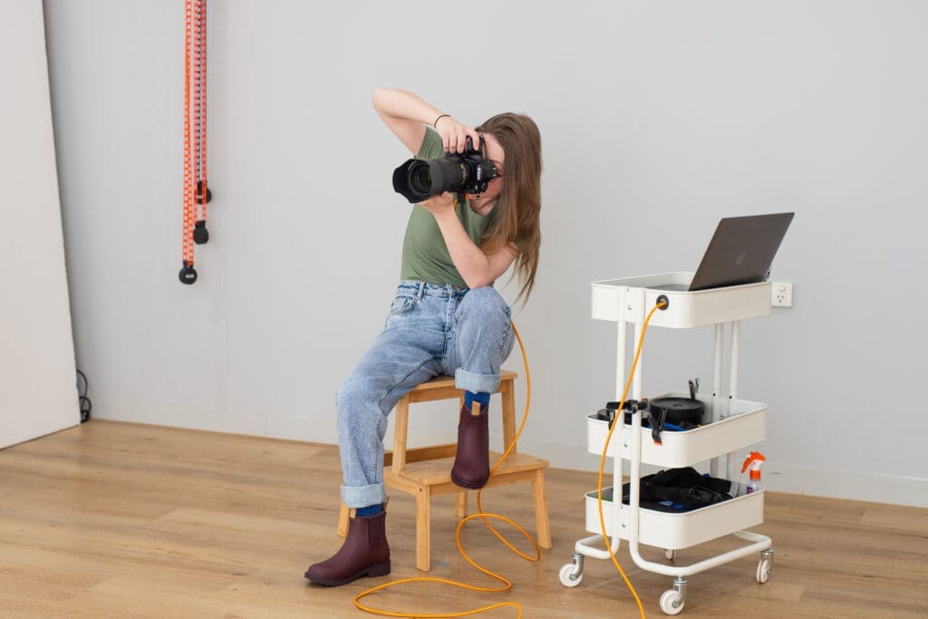 Behind the scenes photograph of Julia in her studio, holding a camera up to her face in-action.